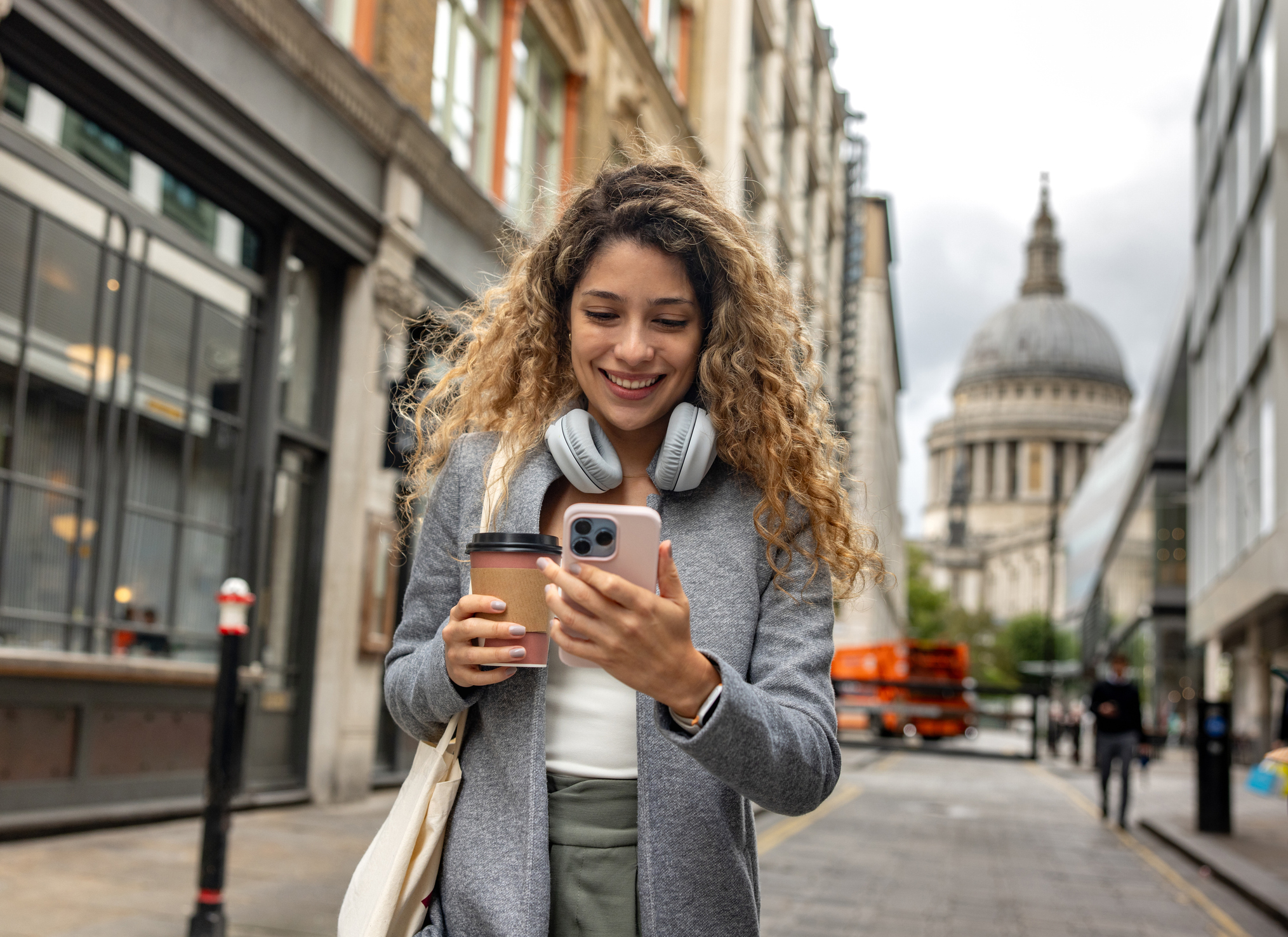 Woman in London using her mobile phone outdoors while drinking a cup of coffee on-the-go