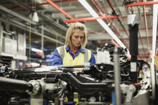 Female production line worker checking a car chassis.